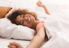 young-woman-smiling-in-bed-stretching-arms-out